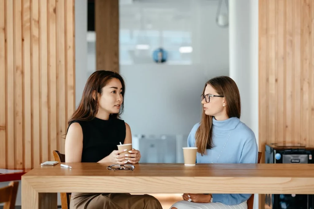 2 vrouwen zitten aan een tafel, drinken koffie en bespreken het werk